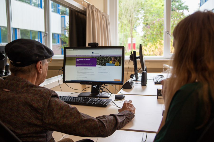 Usability test: a man sitting behind a computer, looking at a website. A researcher sits next to him and observes.